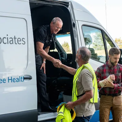 An Injury Care Associates clinician greeting two workers at the mobile unit; one of them has a bandaged forearm.