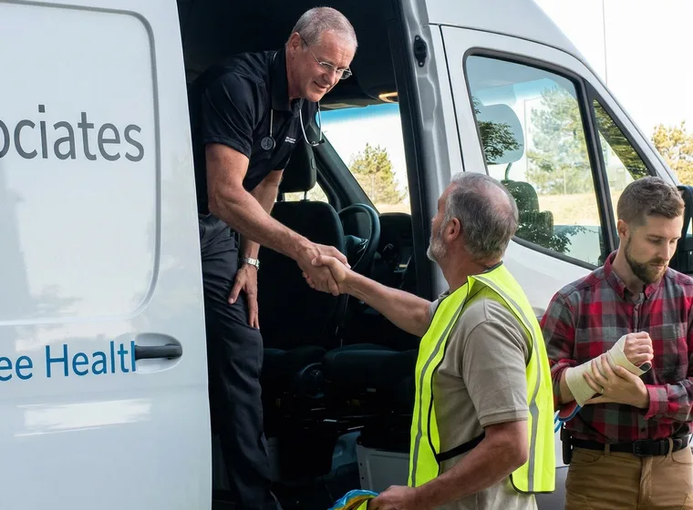 An Injury Care Associates clinician greeting two workers at the mobile unit; one of them has a bandaged forearm.