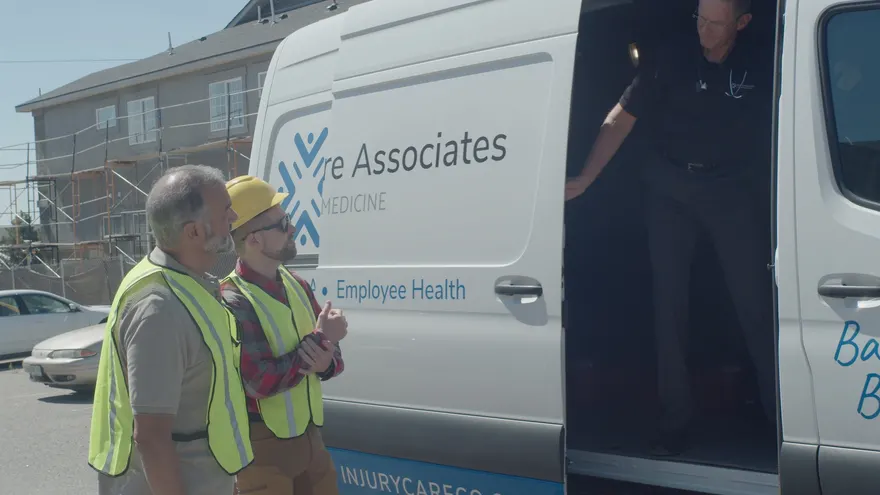 An ICA clinician stepping out of the on-site services van to meet two construction workers in hi-vis vests at a job site