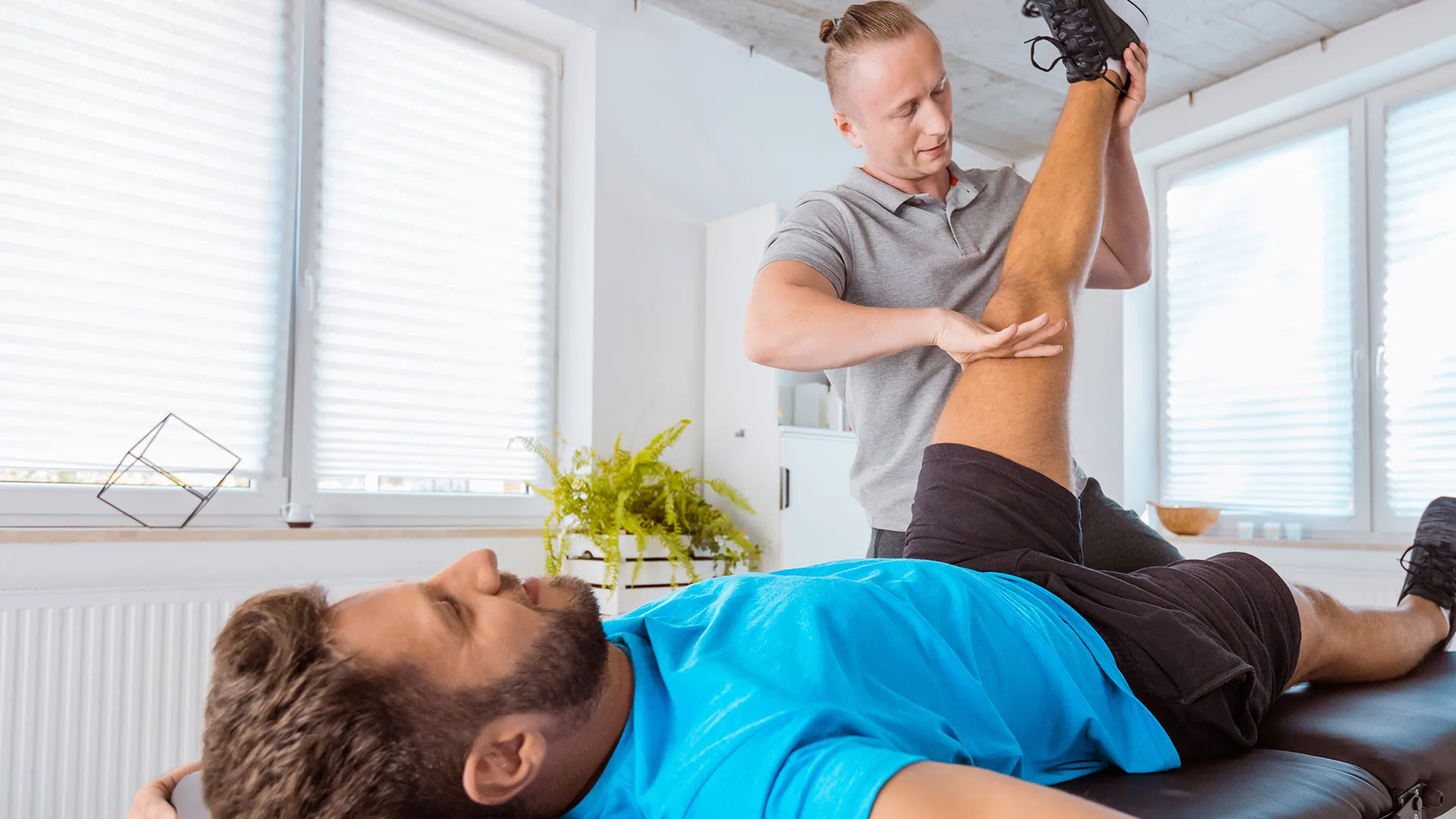 A clinician supporting a patient's leg during a knee range-of-motion assessment on a treatment table.